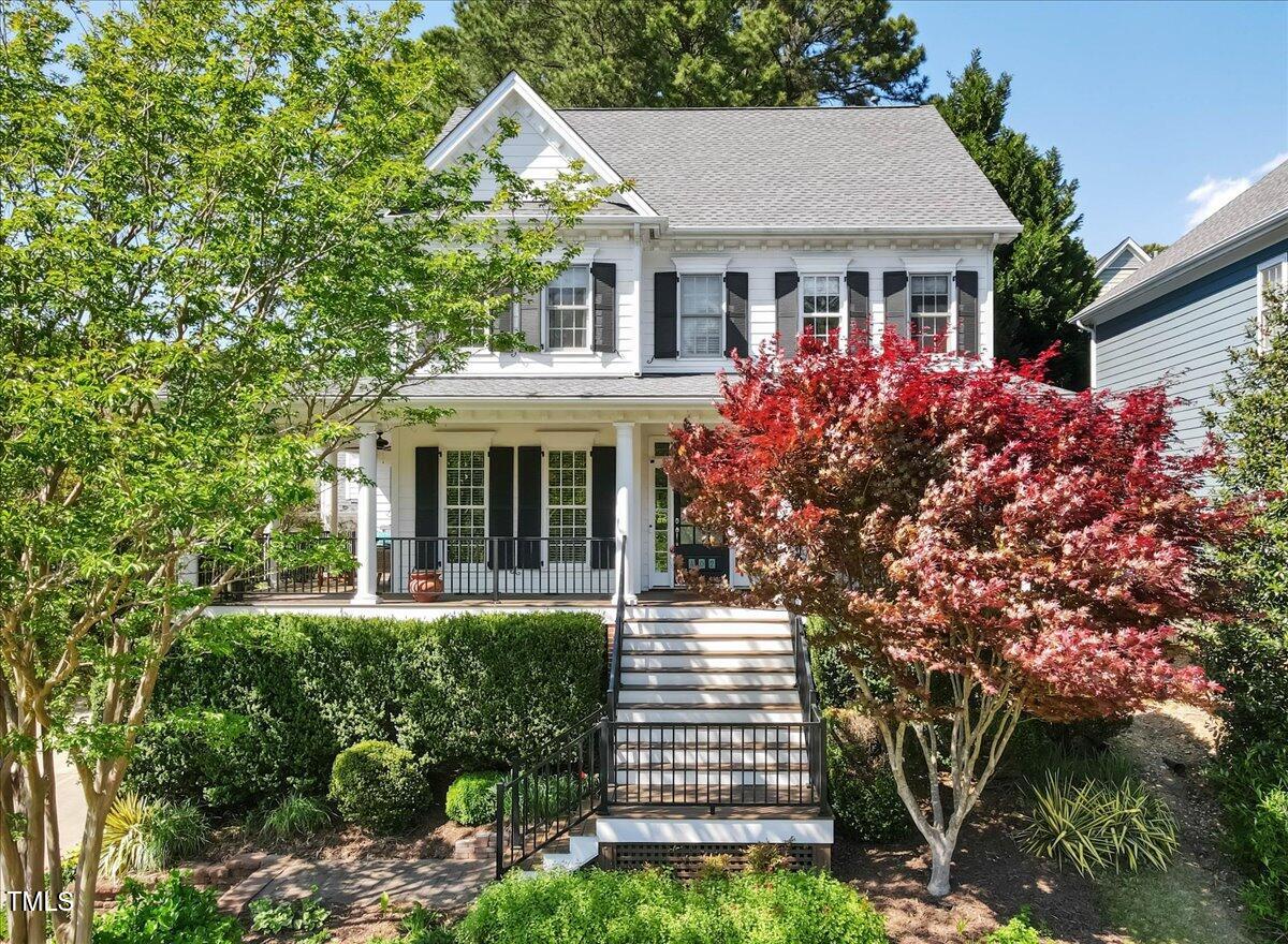 White two-story house with black shutters, a covered porch, and wide front steps amid landscaped trees.