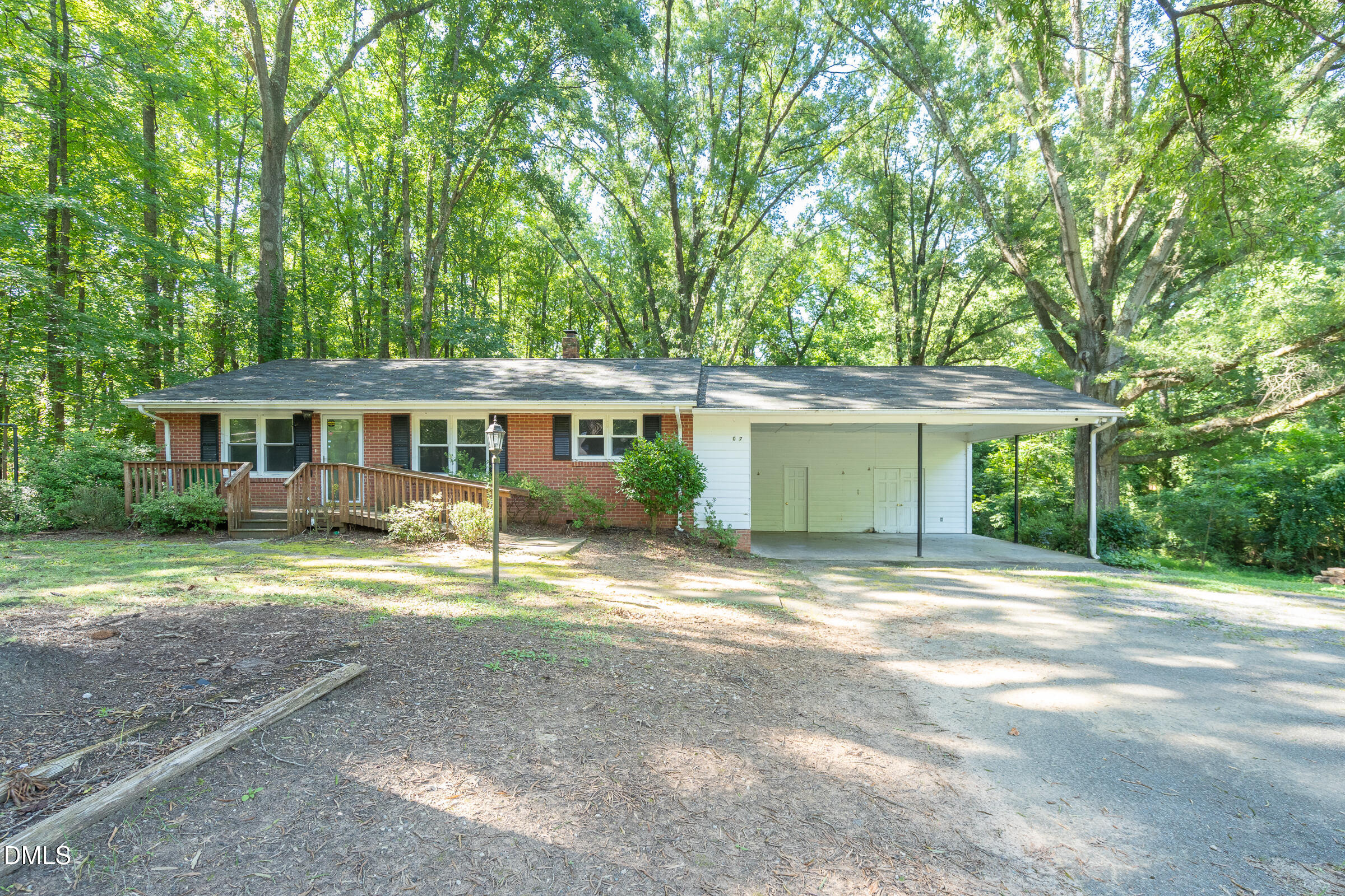 Single-story brick-and-white ranch home with a wooden front ramp and broad carport beneath mature trees.