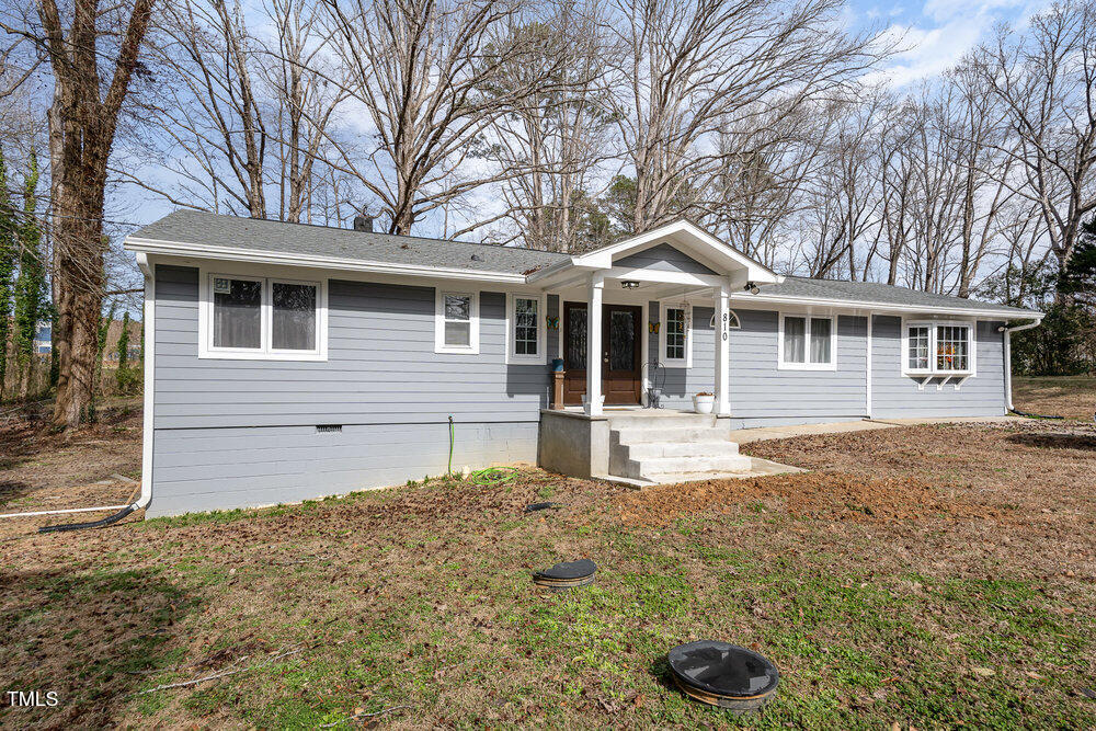 Single-story gray house with a covered entry and concrete steps, surrounded by leafless trees.