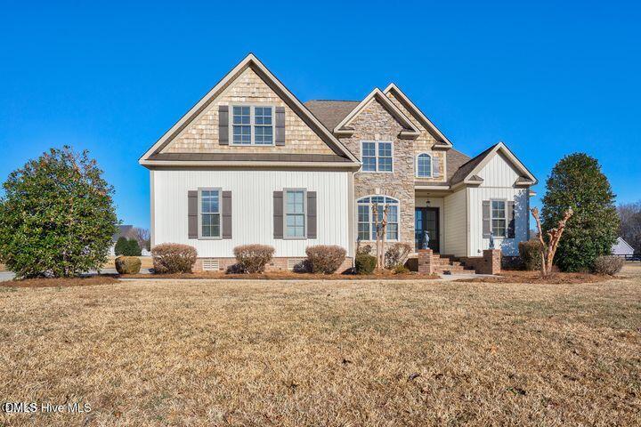 Two-story cream-sided house with stone accents, multiple gables, and a broad lawn.