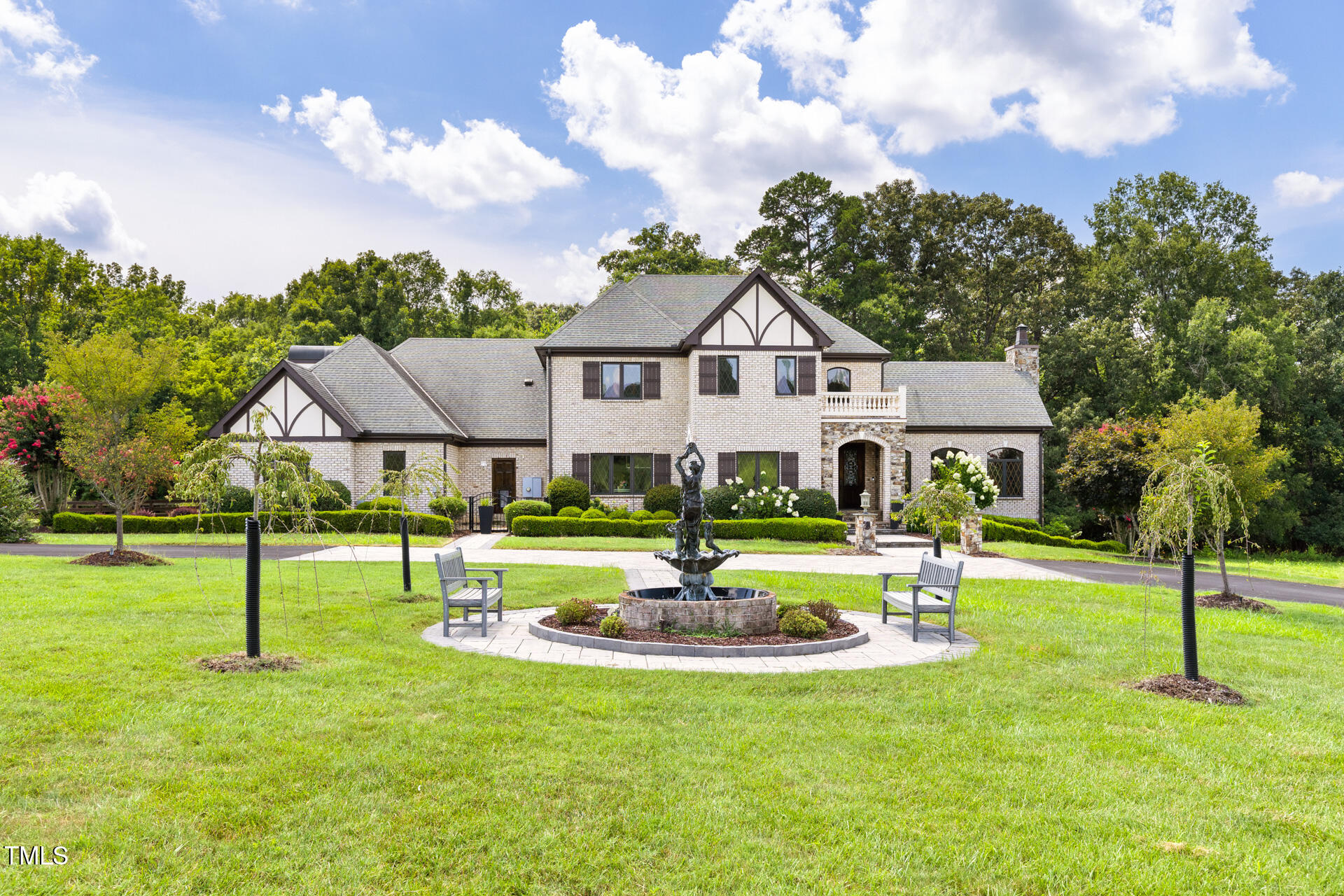 Large brick house with Tudor-style gables, landscaped lawn, and a sculpted fountain in front.