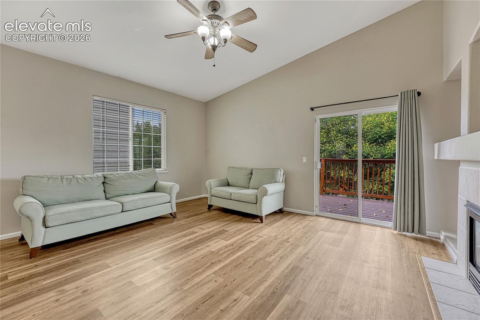 Vaulted ceilings, wood-finish flooring, fireplace with a tile hearth, ceiling fan with light fixture, and sliding glass doors