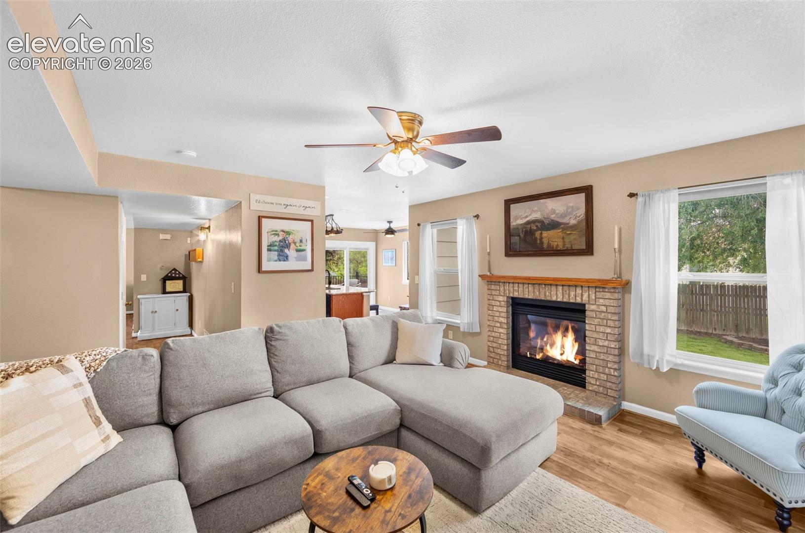 Living area featuring a brick fireplace with a wood mantel, wood-finish flooring, and multiple windows