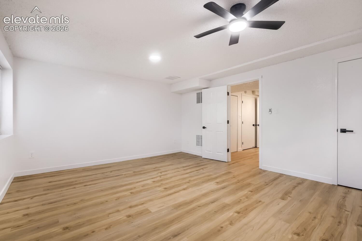 Neutral interior space featuring wood-finish flooring, a ceiling fan with integrated light fixture, and matte black door hardware