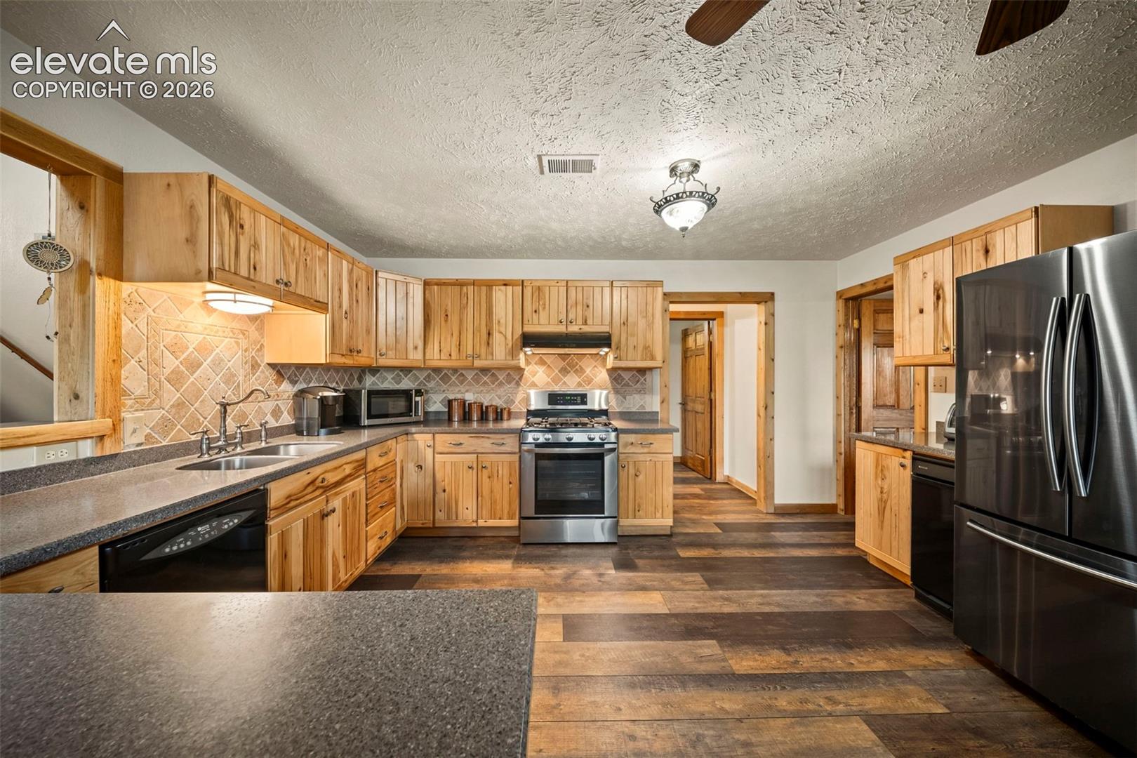 Kitchen featuring solid wood cabinetry, stone-finish countertops, tile backsplash, stainless steel appliances, and wood-finish flooring