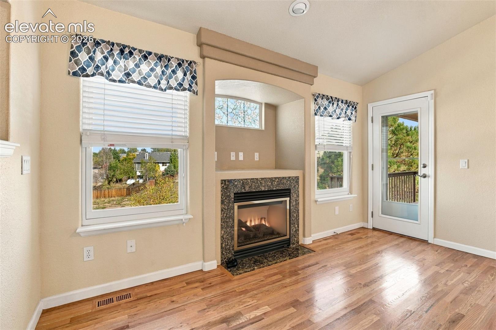 Wood-finish flooring, fireplace with stone surround, recessed media niche, and glass-paneled exterior door