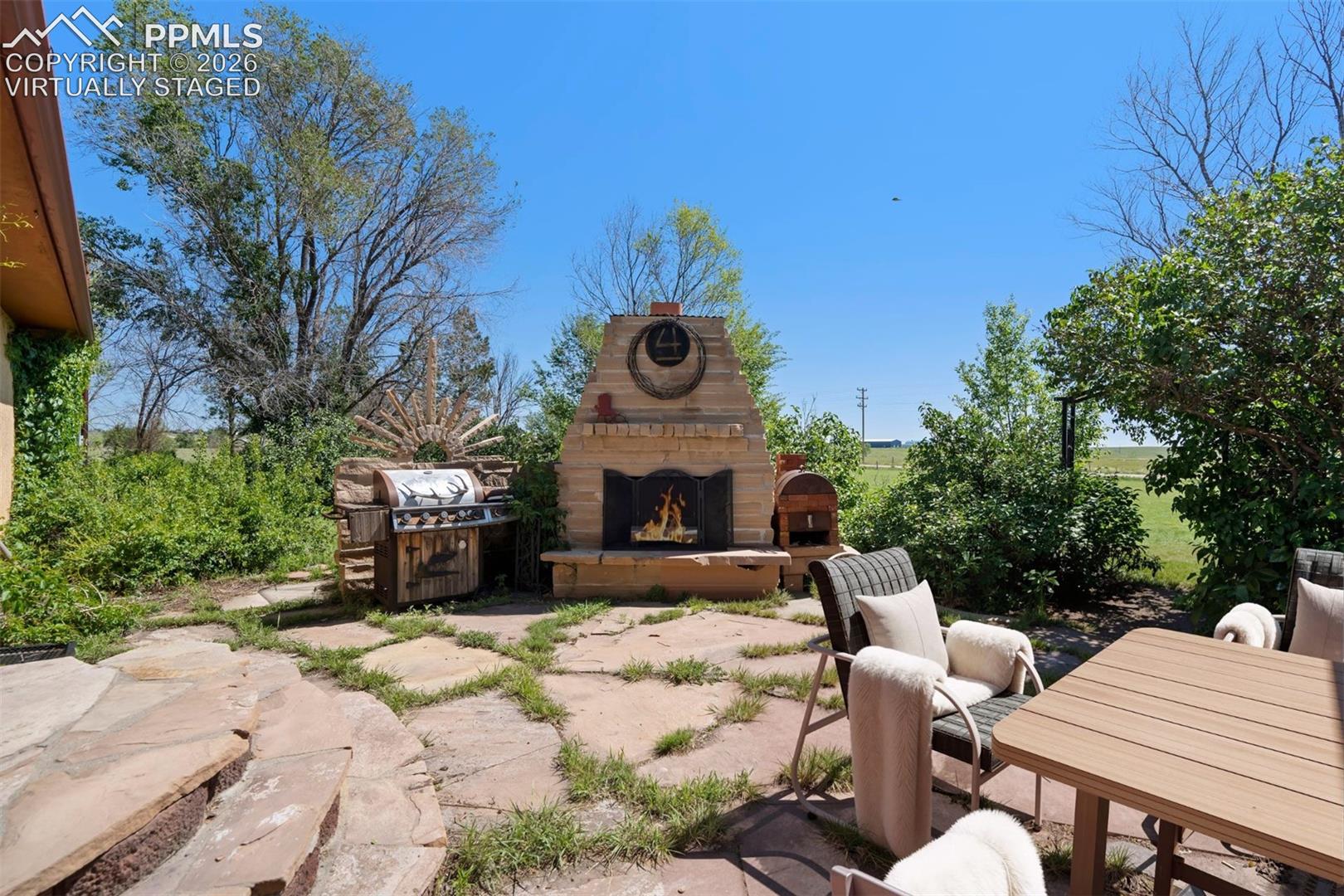 virtually staged Stone patio featuring an outdoor fireplace with a prominent hearth, a built-in outdoor grill, and irregular flagstone pavers