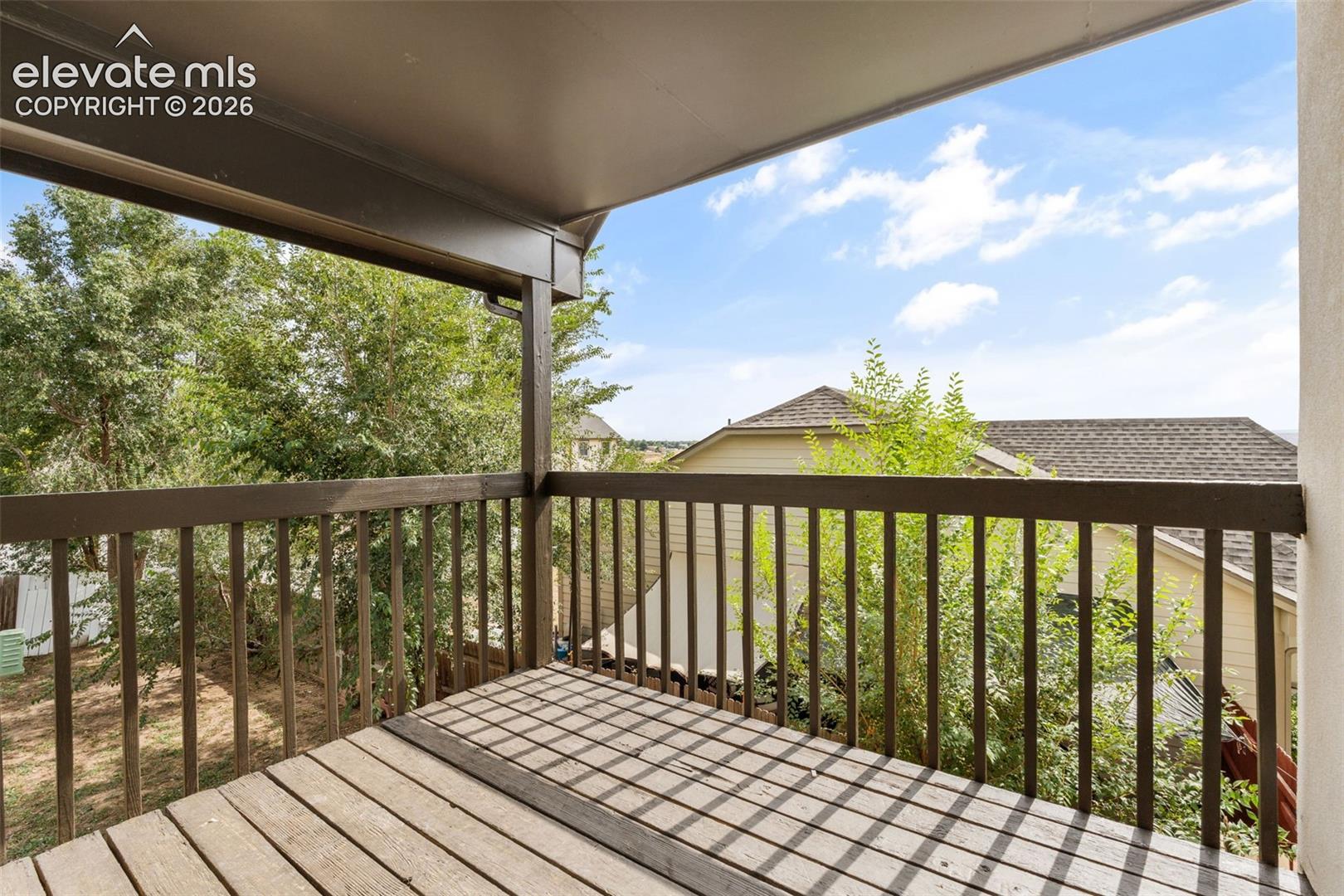 Covered balcony featuring wood-plank decking and a wooden railing