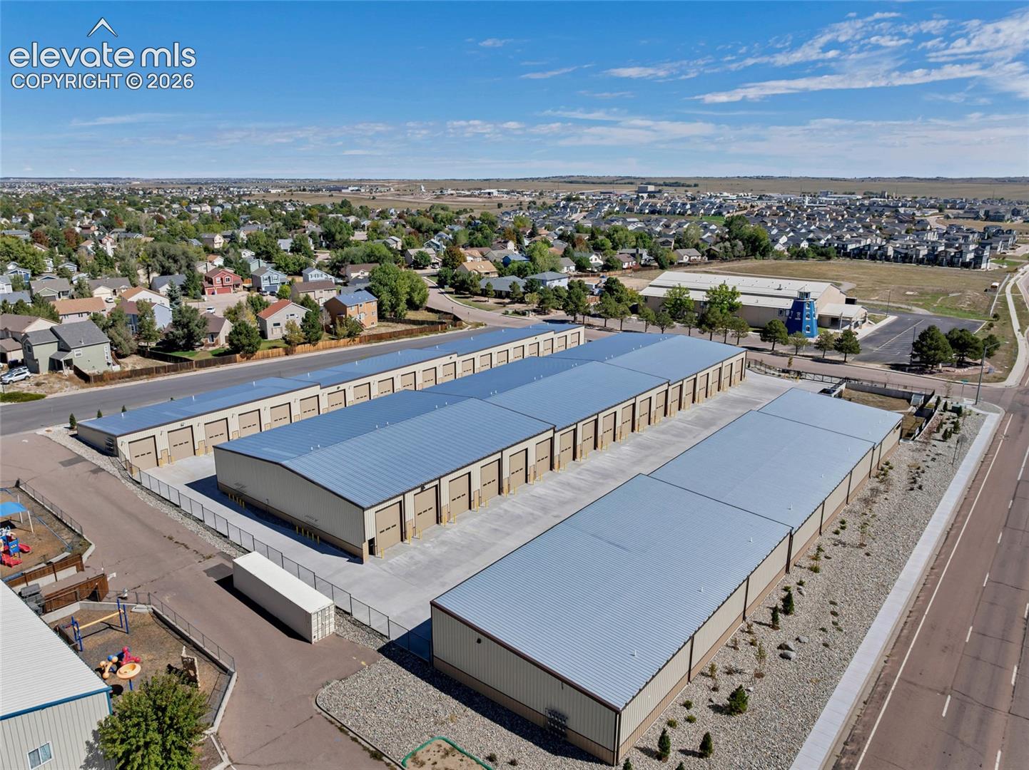 Multiple storage buildings with metal roofs and roll-up doors, paved driveways, and perimeter fencing