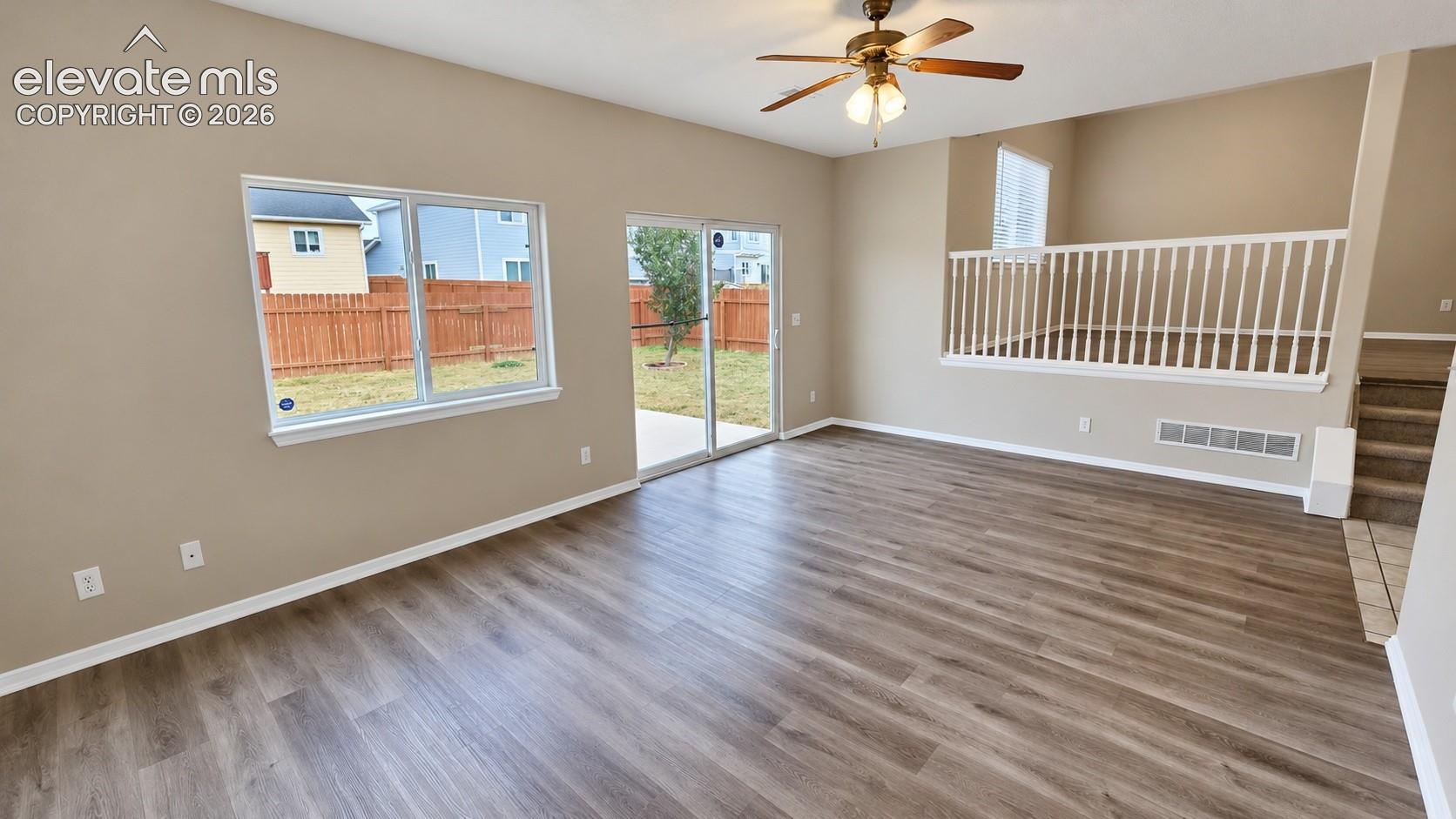 Living space featuring wood-finish flooring, vaulted ceilings, sliding glass door, white railing with open balusters, and a ceiling fan with light fixture