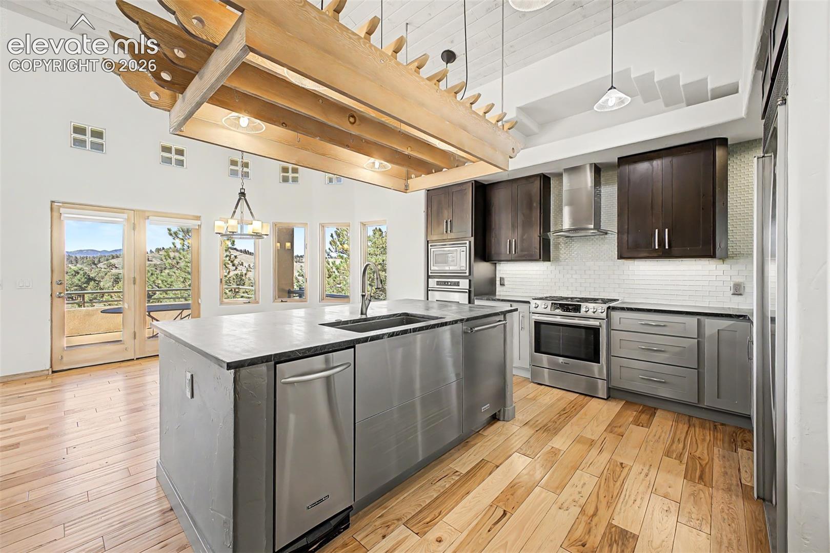 Gourmet kitchen with stainless steel appliances, a center island featuring an integrated sink, wood-finish flooring, and a vaulted ceiling with exposed beam accents
