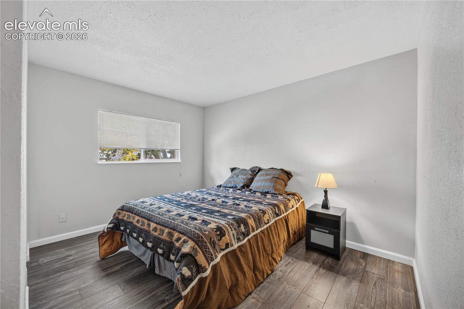 Room featuring wood-finish flooring, neutral walls, and a single-pane window with a fitted roller shade