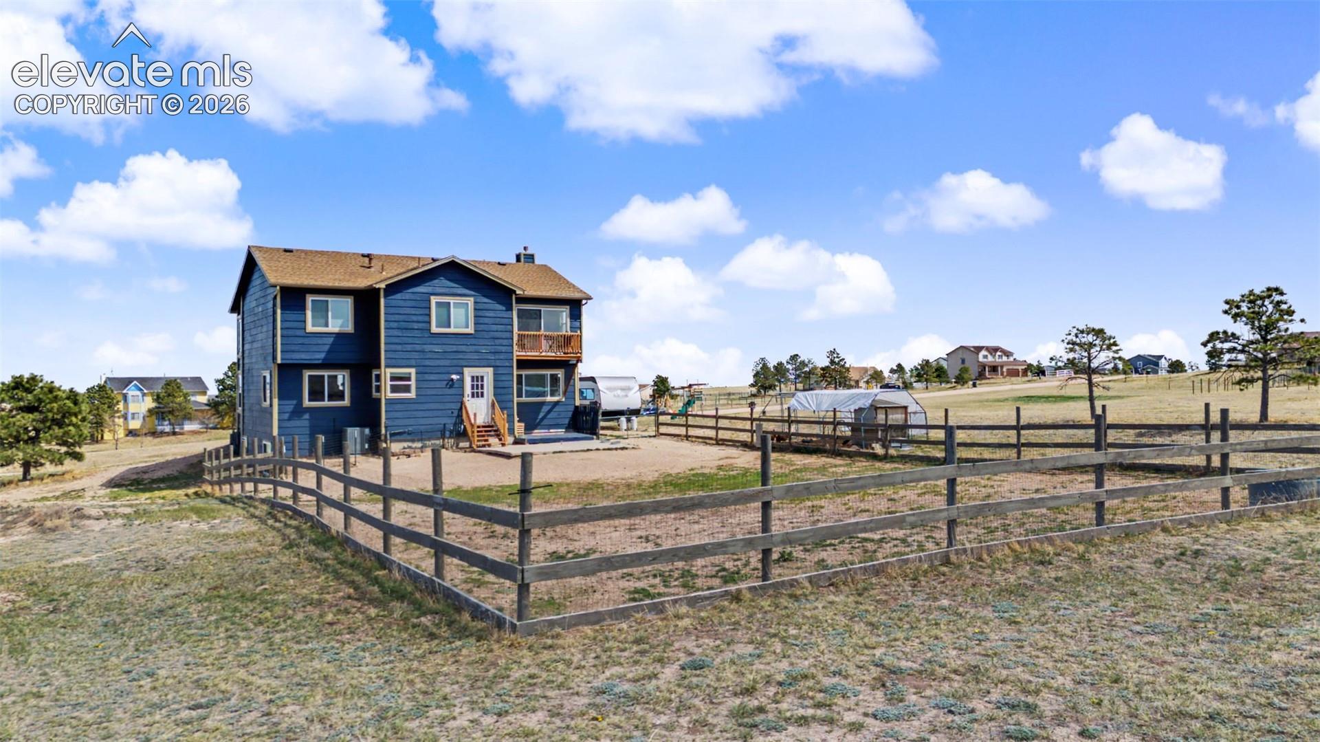 Two-story residence featuring blue horizontal siding, an upper-level balcony, a paved rear patio, and a fenced perimeter