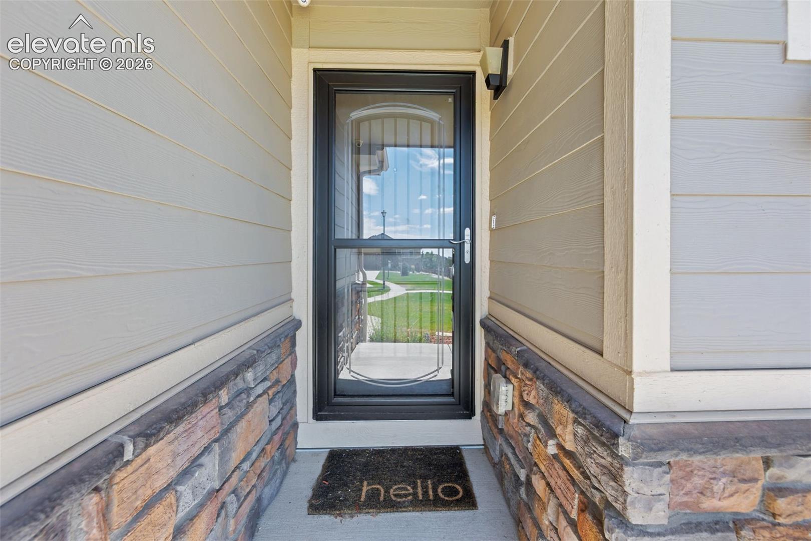 Entryway featuring horizontal siding, stone veneer accents, and a full-light storm door