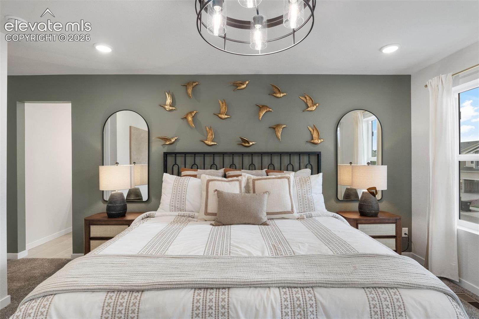 primary bedroom with green accent wall, metal bird wall art, and matching arched mirrors over bedside tables