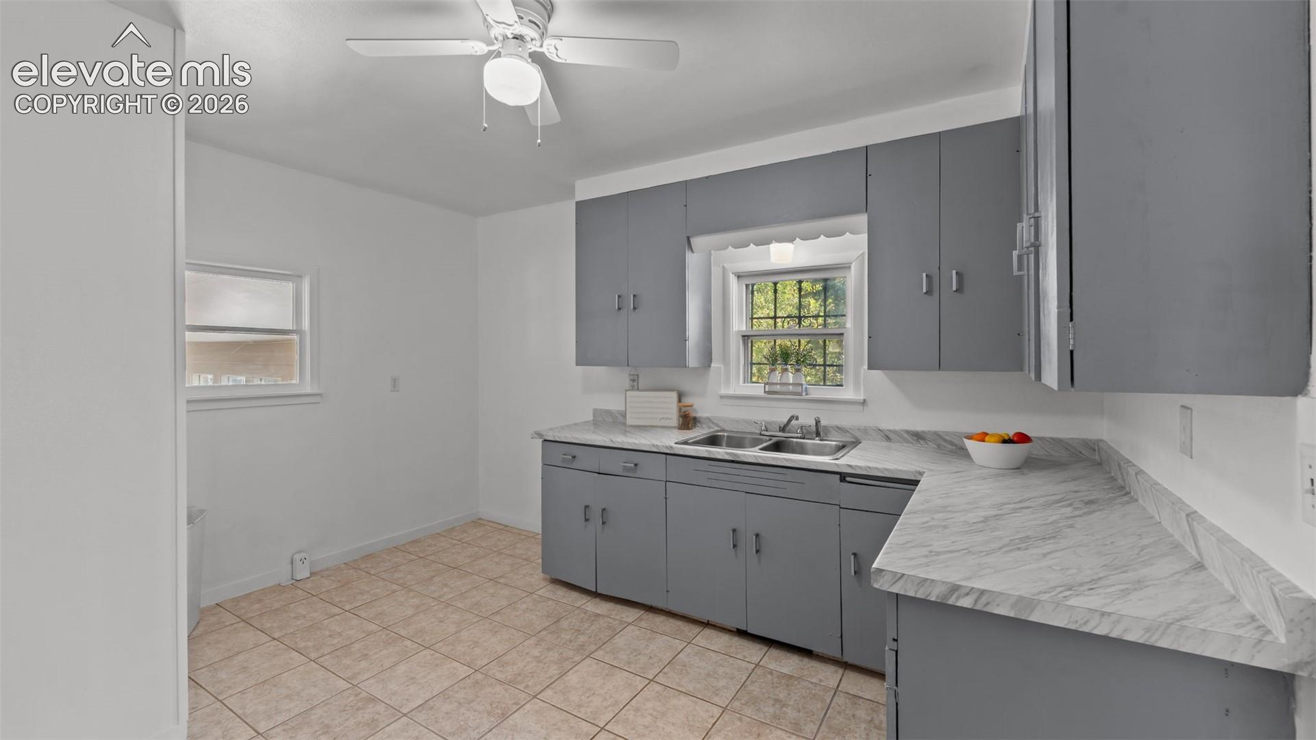 Kitchen featuring tile flooring, gray cabinetry, laminate countertops, a double basin sink, and a ceiling fan