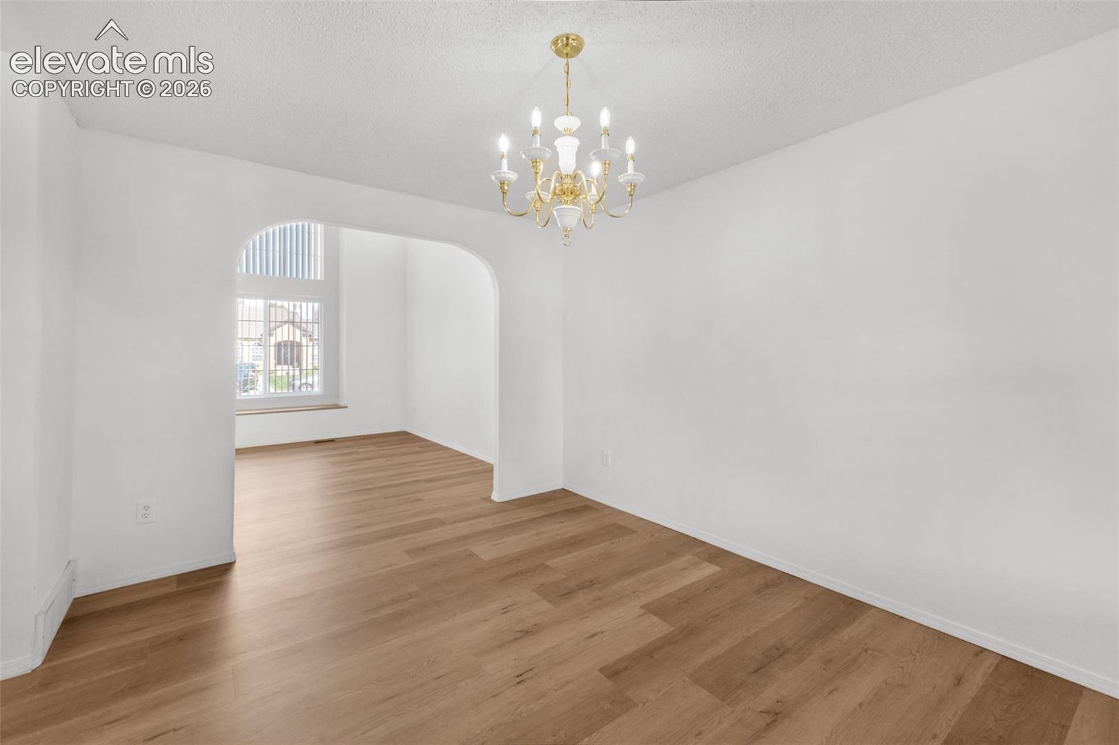 Recessed lighting and a decorative chandelier illuminate the space, featuring light wood-finish flooring and an arched entryway