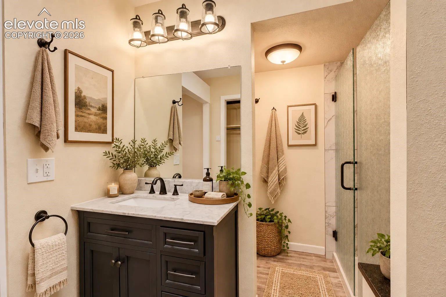 Dark-toned vanity with a stone countertop, integrated undermount sink, multi-light industrial-style vanity fixture, and walk-in shower with textured glass enclosure. AI-Enhanced – furniture/decor digitally added