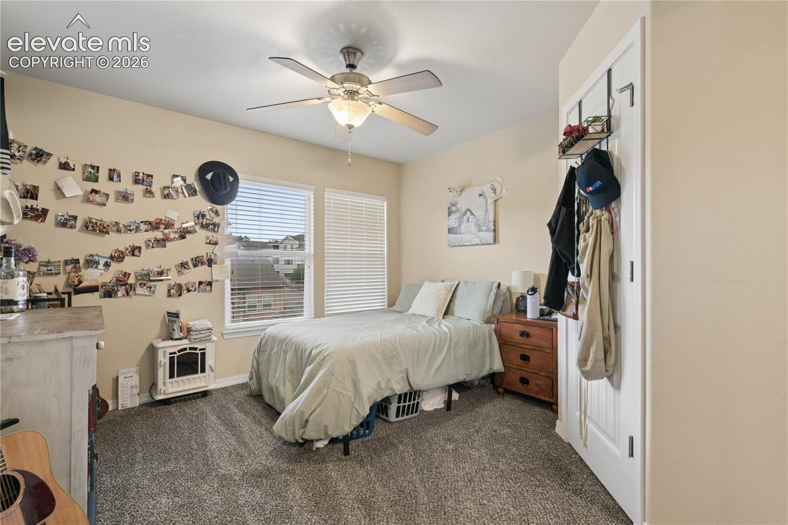 Neutral-toned room featuring a ceiling fan with integrated lighting, two windows with horizontal blinds, and a door with an over-the-door storage rack
