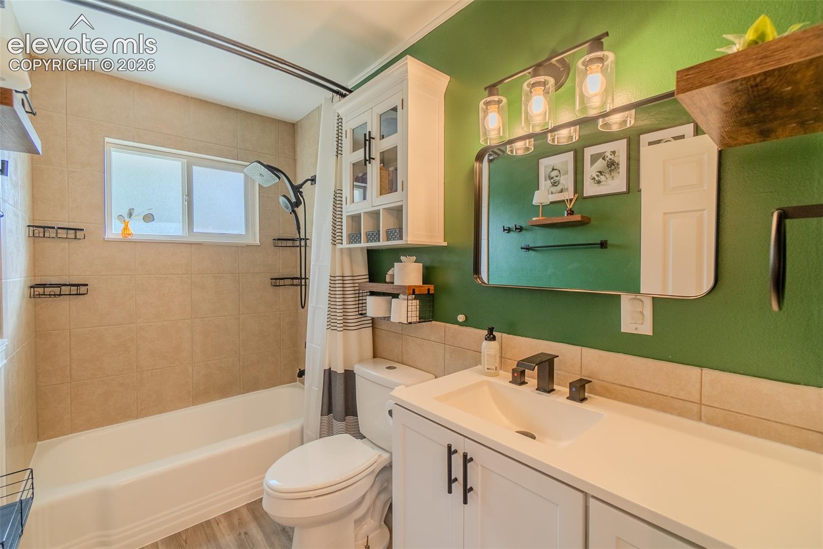 Bathroom featuring a white vanity cabinet with a rectangular basin and matte black faucet, wall-mounted upper storage cabinetry, an oversized rectangular mirror with a black frame, and a bathtub with tile surround