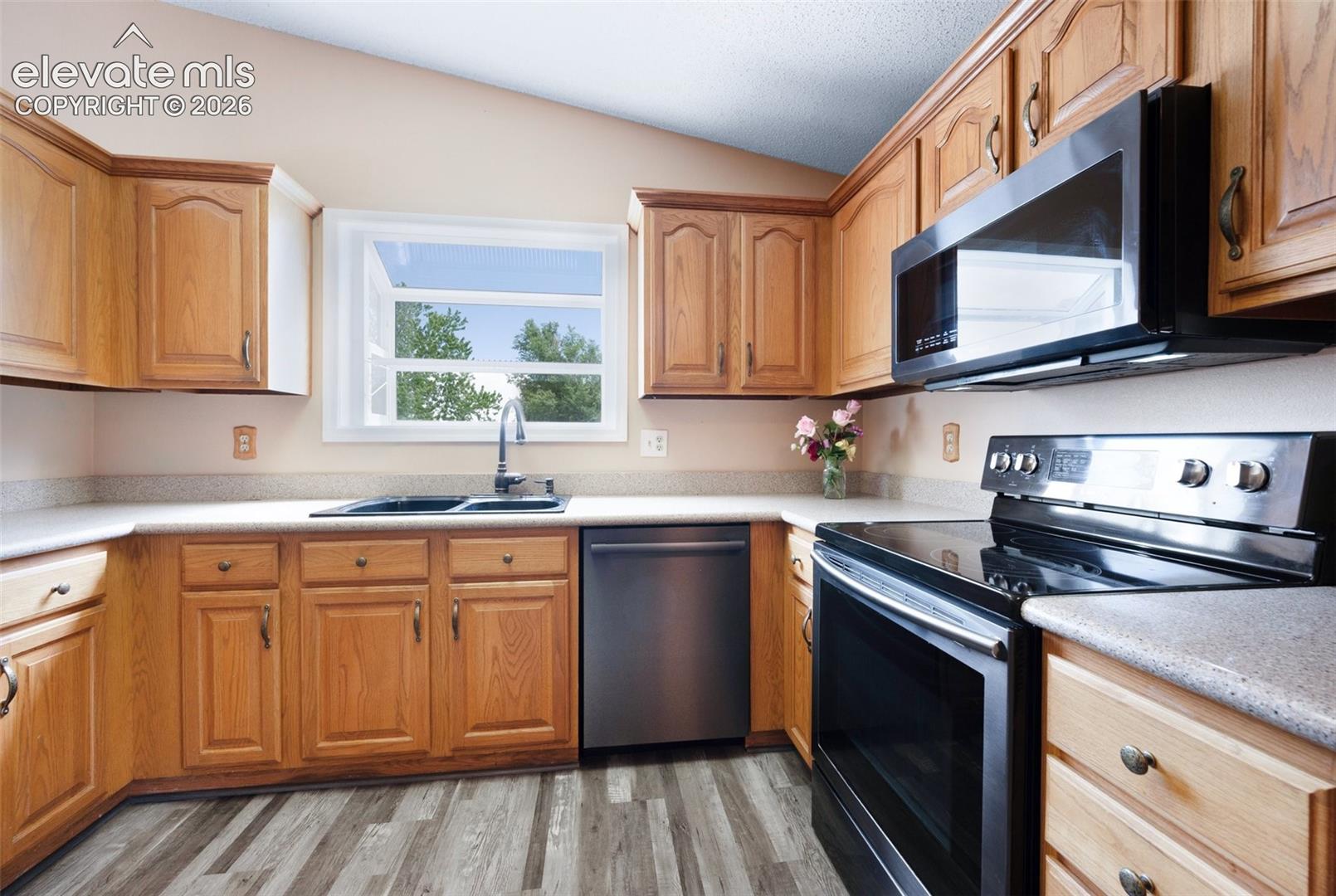 Kitchen with appliances with stainless steel finishes, a sink, vaulted ceiling, light wood-style floors, and light countertops