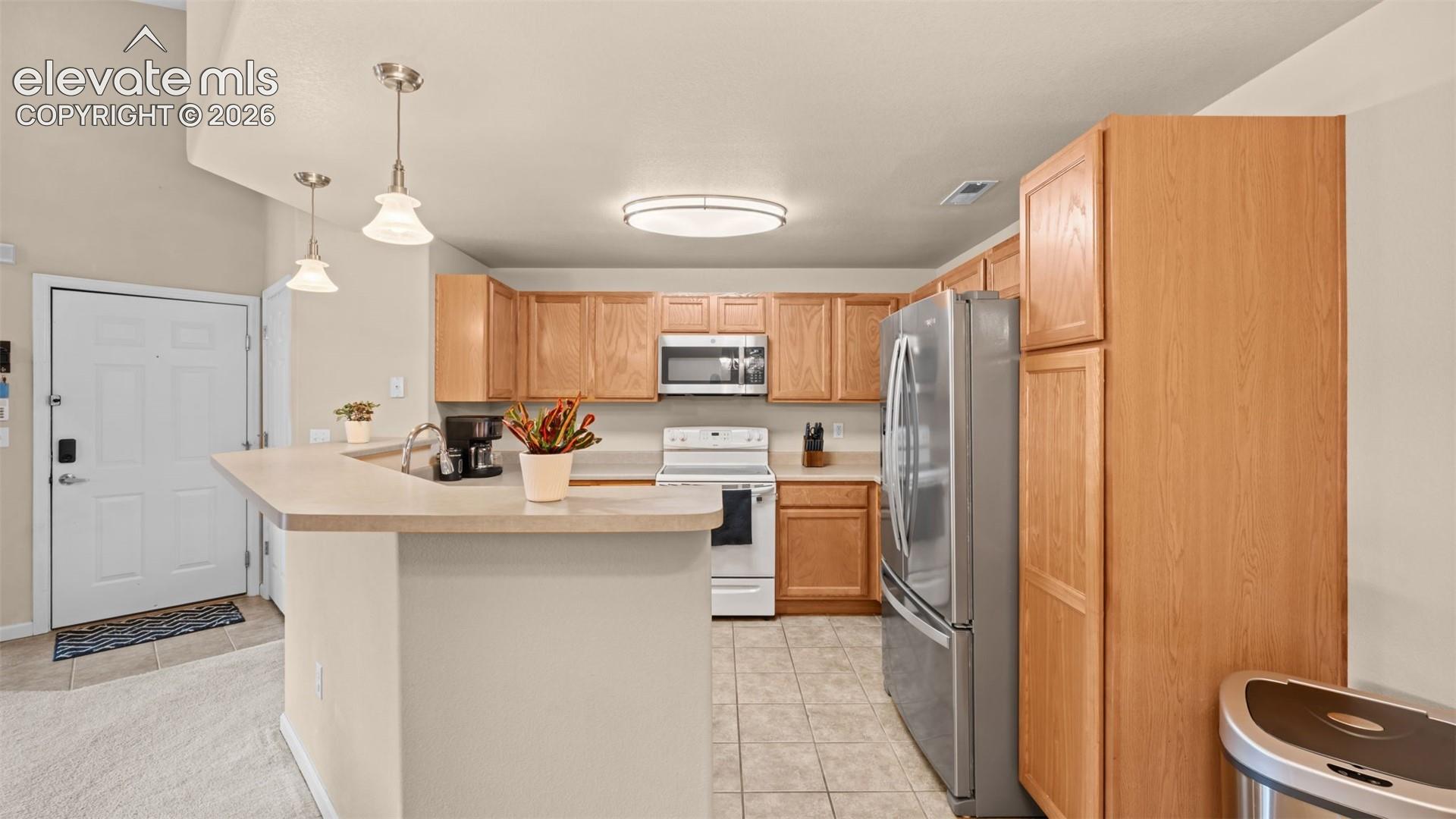 Open-concept kitchen featuring light wood-finish cabinetry, stainless steel appliances, a breakfast bar, and tile flooring