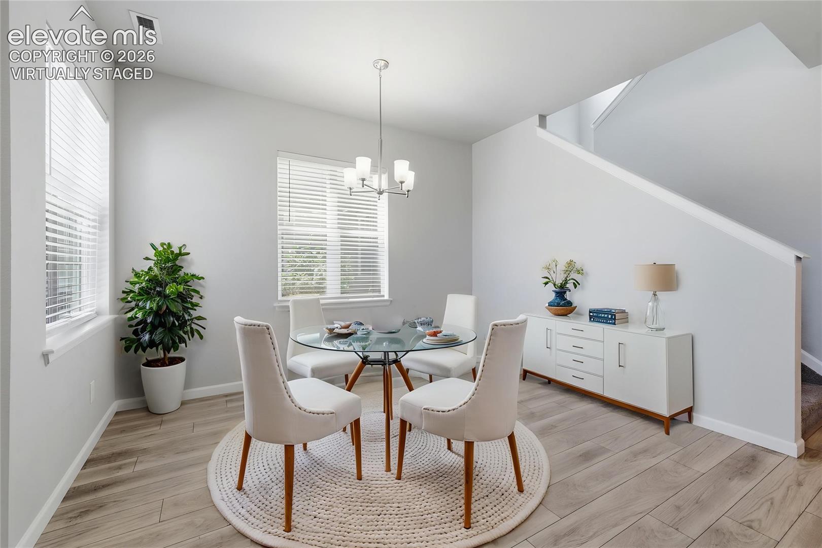 Open-concept dining area featuring wood-finish flooring and multiple windows with blinds -- virtually staged. 