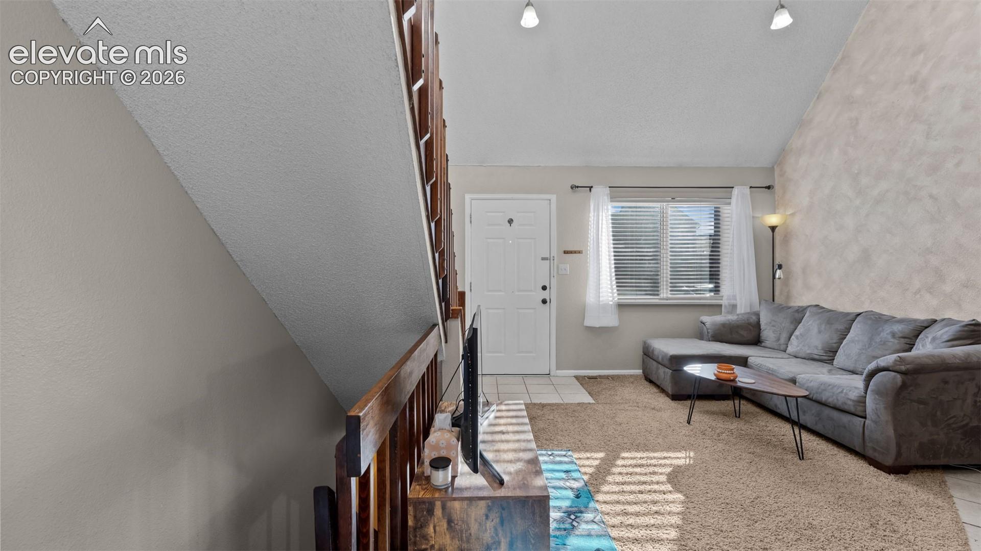 Vaulted ceiling, interior staircase with a wood railing, and an exterior entry door with a multi-pane window