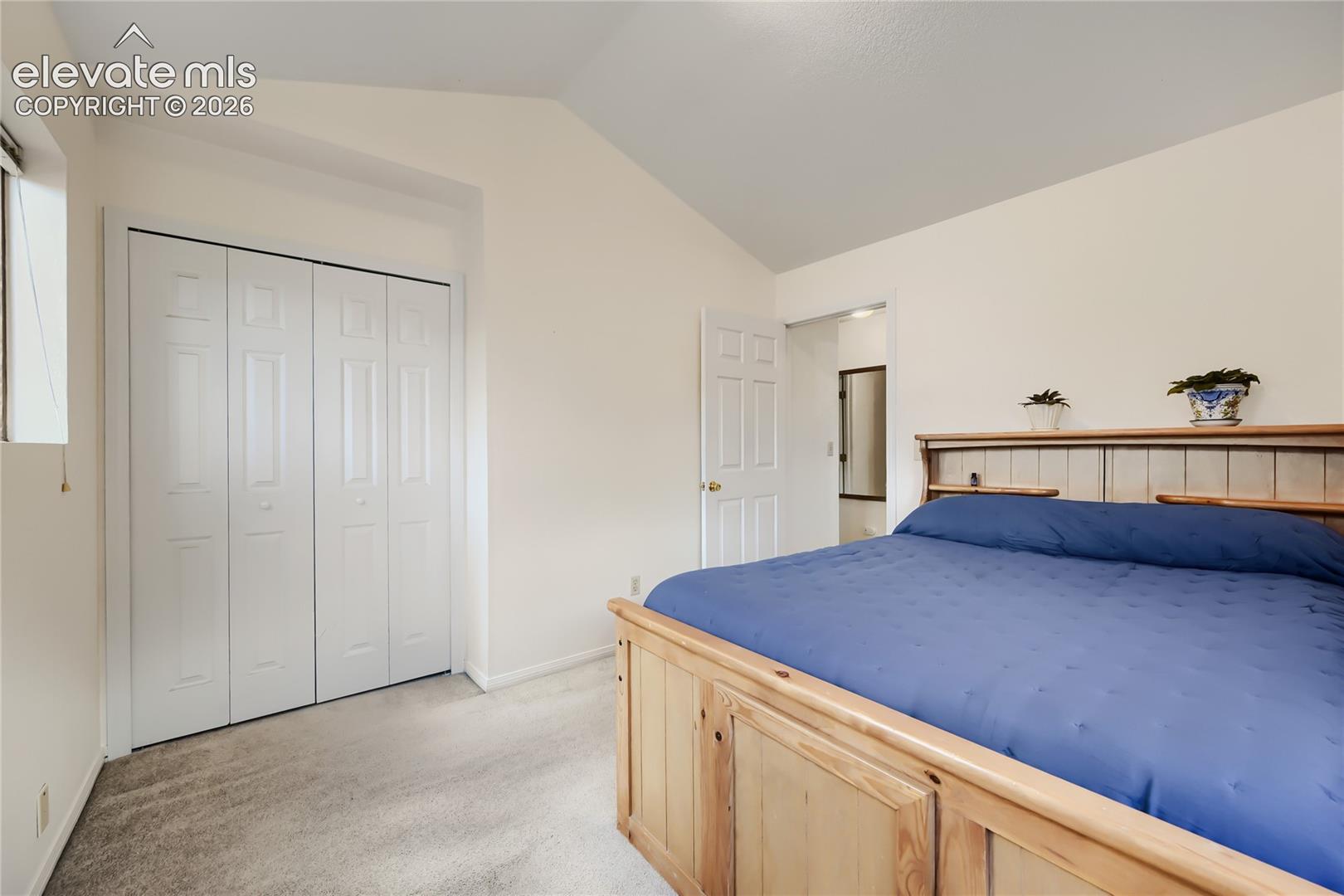Vaulted ceiling, bi-fold closet doors, wall-to-wall carpeting, and wood-finish door