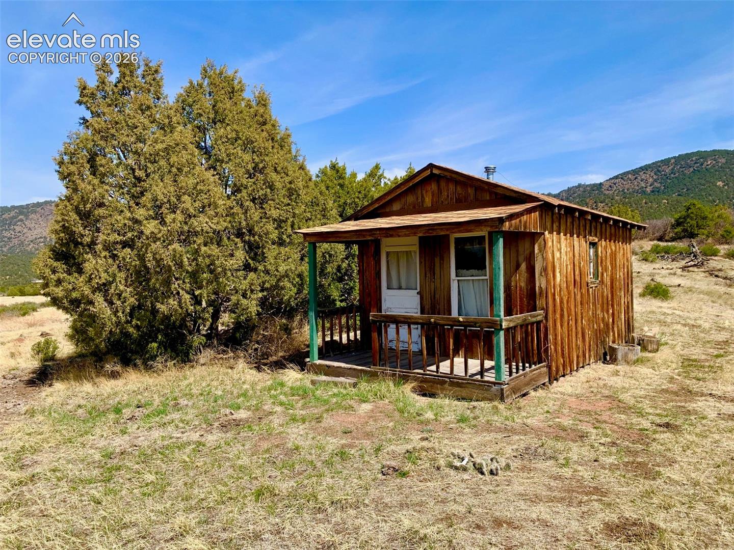 Rustic wood-sided cabin featuring a covered front porch with railings and a mountain landscape setting