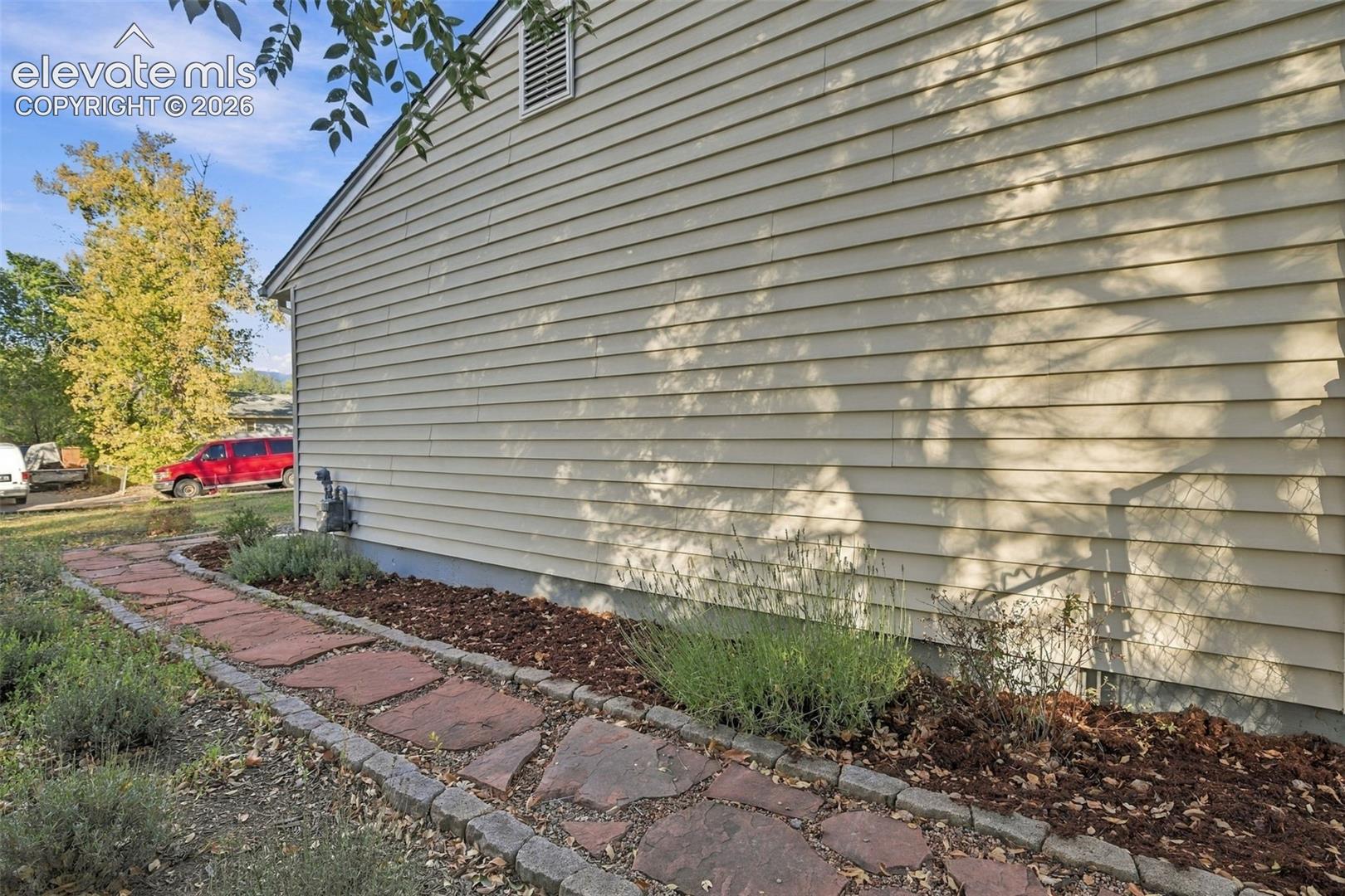 Light-colored horizontal siding exterior featuring a flagstone walkway bordered by stone pavers and mulched garden beds