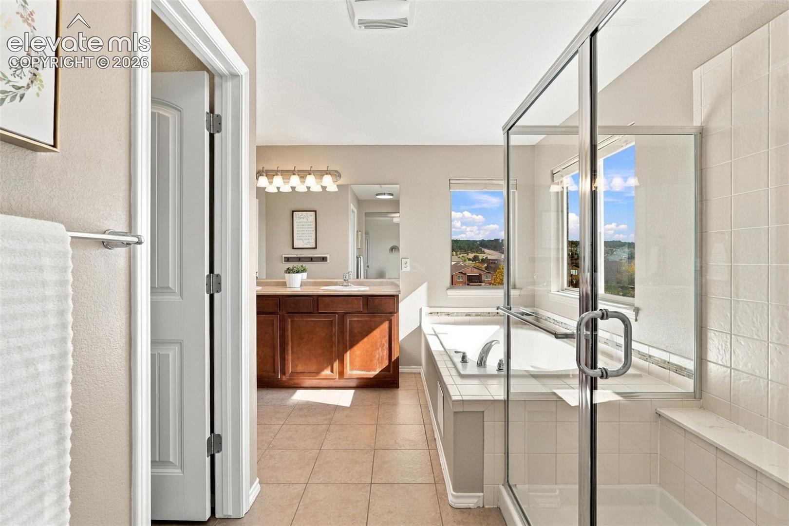 Bathroom featuring a soaking tub, glass-enclosed shower with tiled surround, wooden cabinetry, and dual-basin vanity