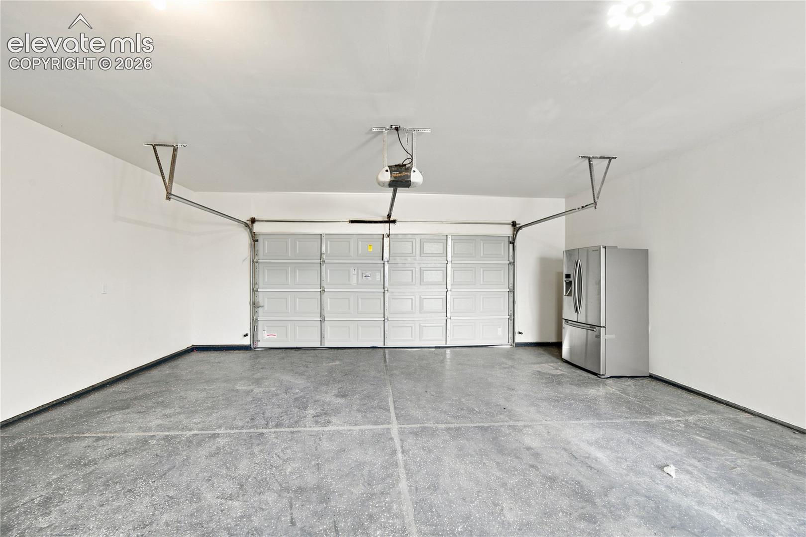 Two-car garage featuring a sectional overhead door with an automatic opener, concrete flooring, and bright overhead lighting