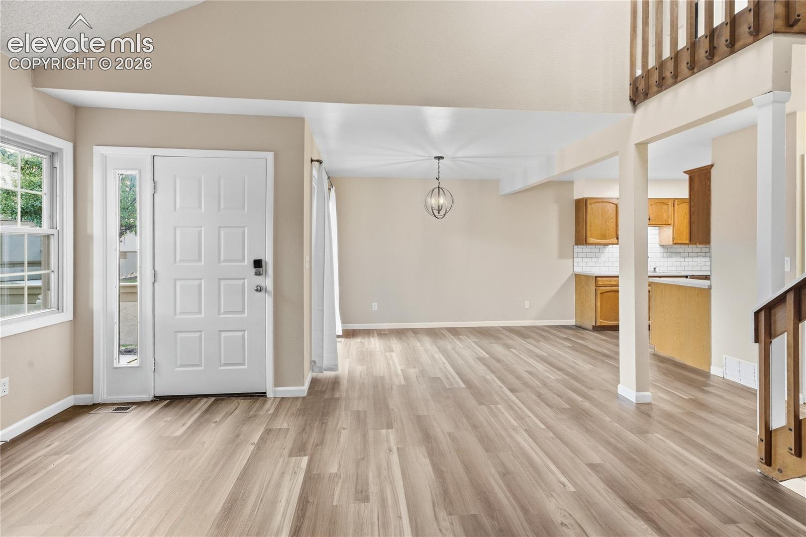 Vaulted ceiling, wood-finish flooring, entry door with sidelight, open-concept design, and an overhead light fixture