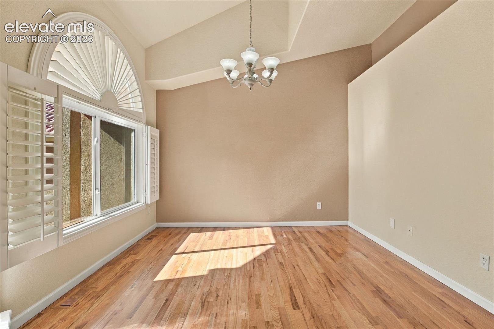 Vaulted ceilings, wood-finish flooring, arch-top window with plantation shutters, and multi-arm chandelier