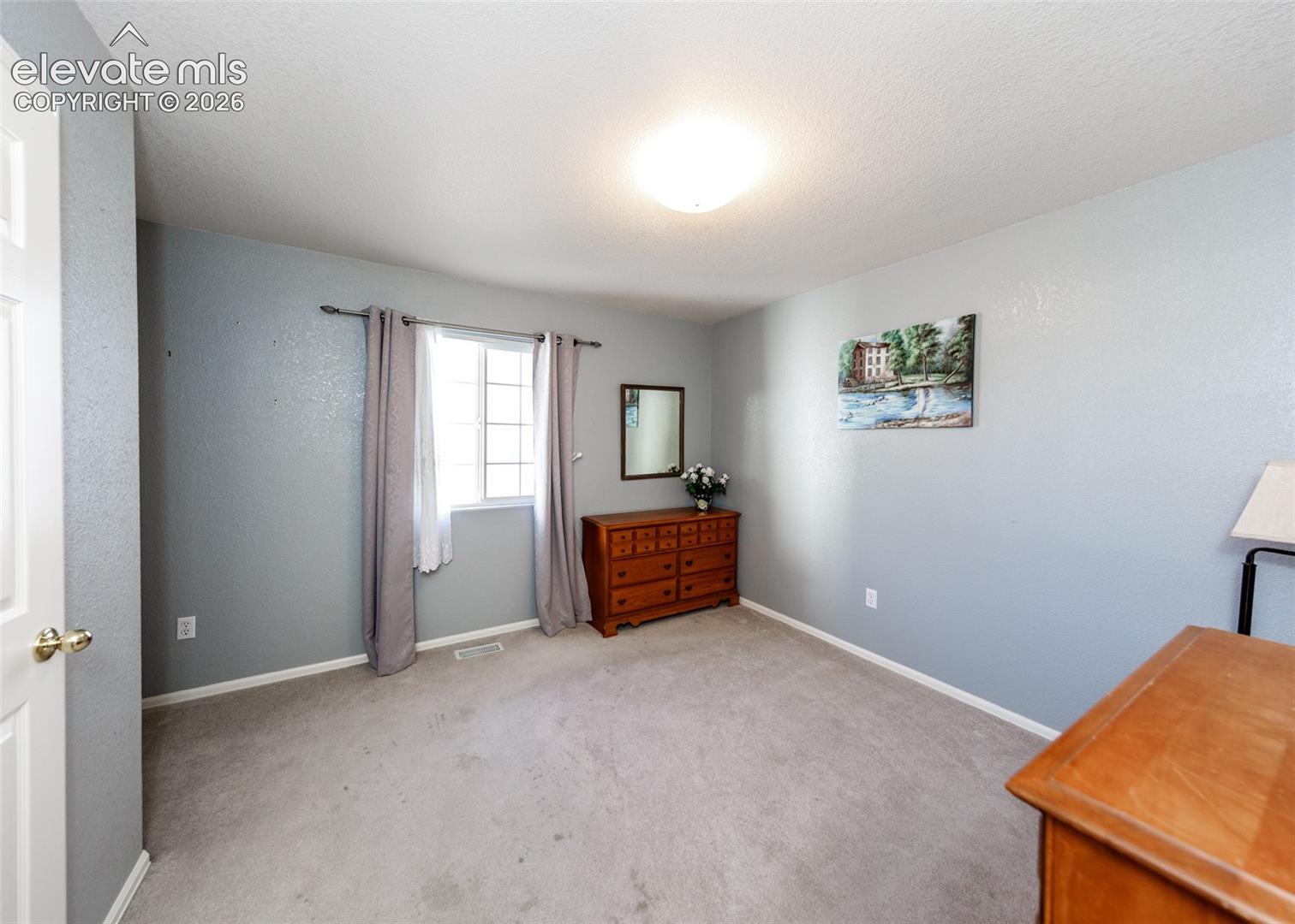 Neutral-toned interior space featuring light gray walls, wall-to-wall carpeting, a single-hung window, and a central ceiling-mounted light fixture