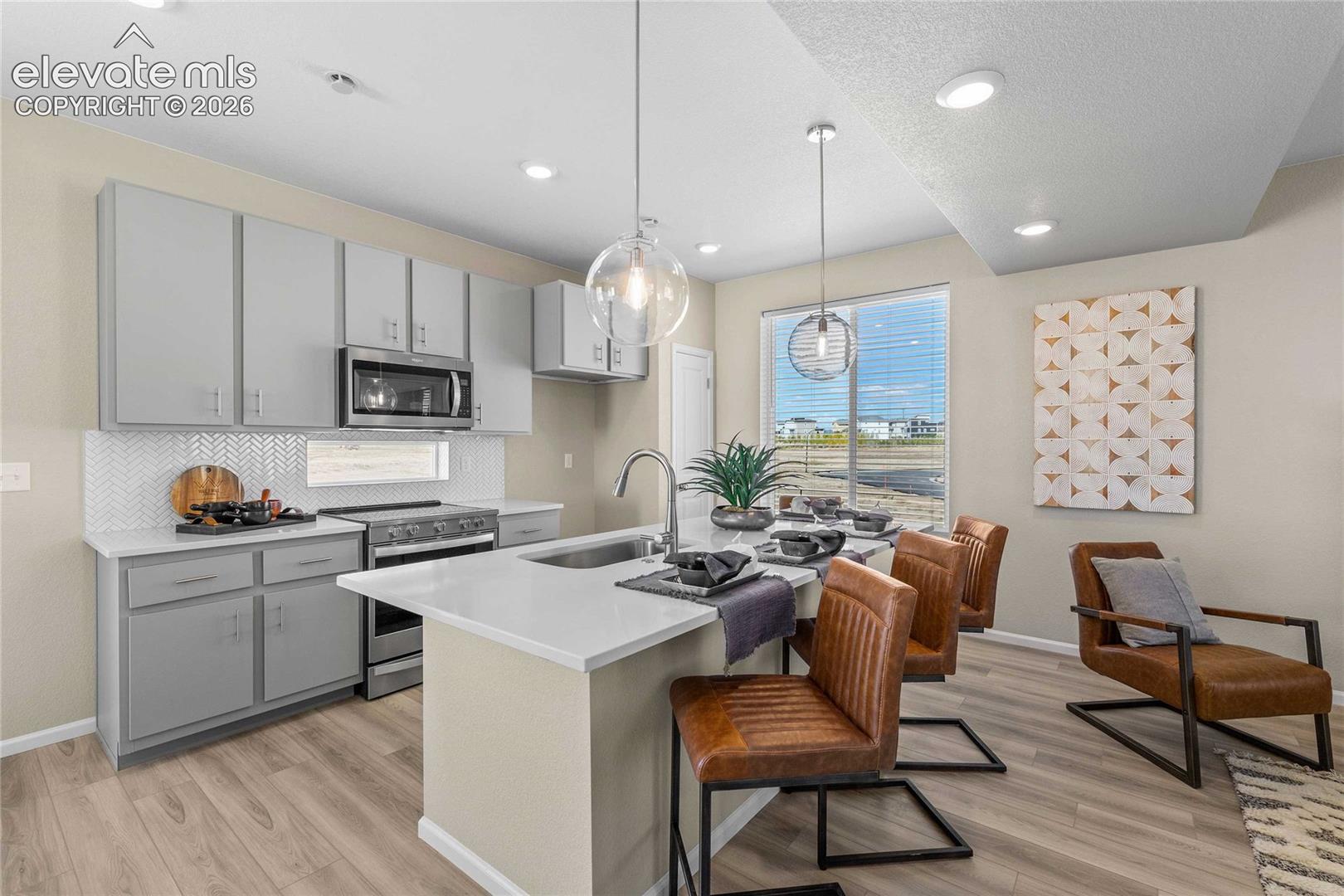 Contemporary kitchen featuring light gray cabinetry, stainless steel appliances, a white herringbone backsplash, and a central island with a sink
*photos of a model home*