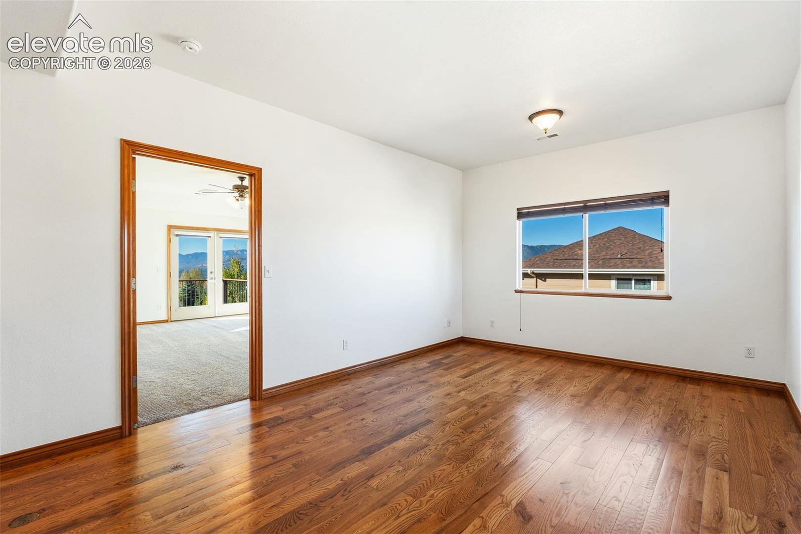 Interior space featuring wood-finish flooring, white walls, wood-trimmed door frame, flush-mount lighting, and a window with mountain scenery
