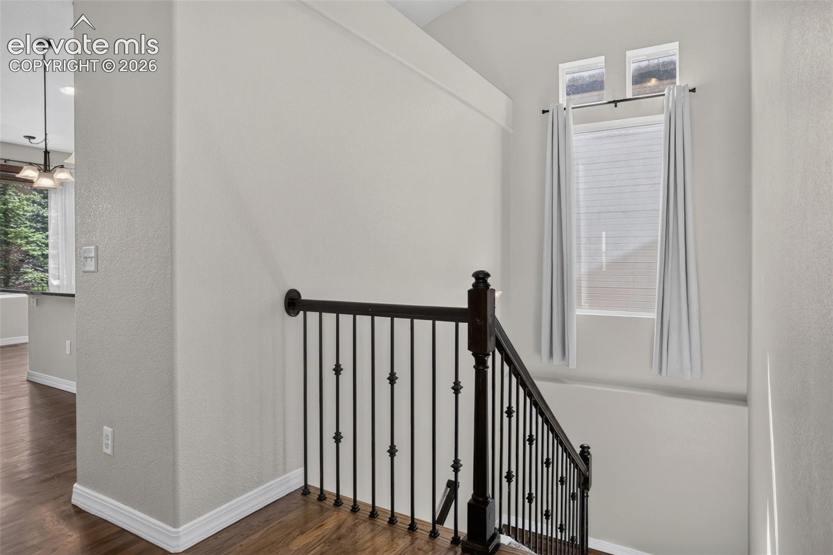 Wood-finish flooring, staircase with dark wood newel post and wrought iron balusters, high ceilings, multiple windows, and recessed lighting