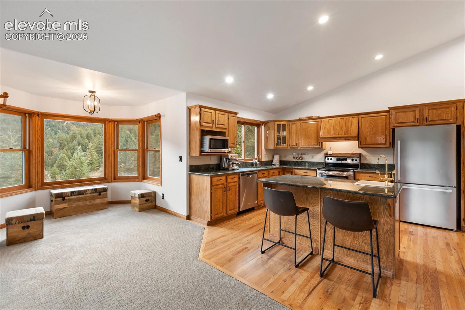 Kitchen featuring wood cabinetry, stone countertops, a center island, recessed lighting, and a bay window with a mountain backdrop