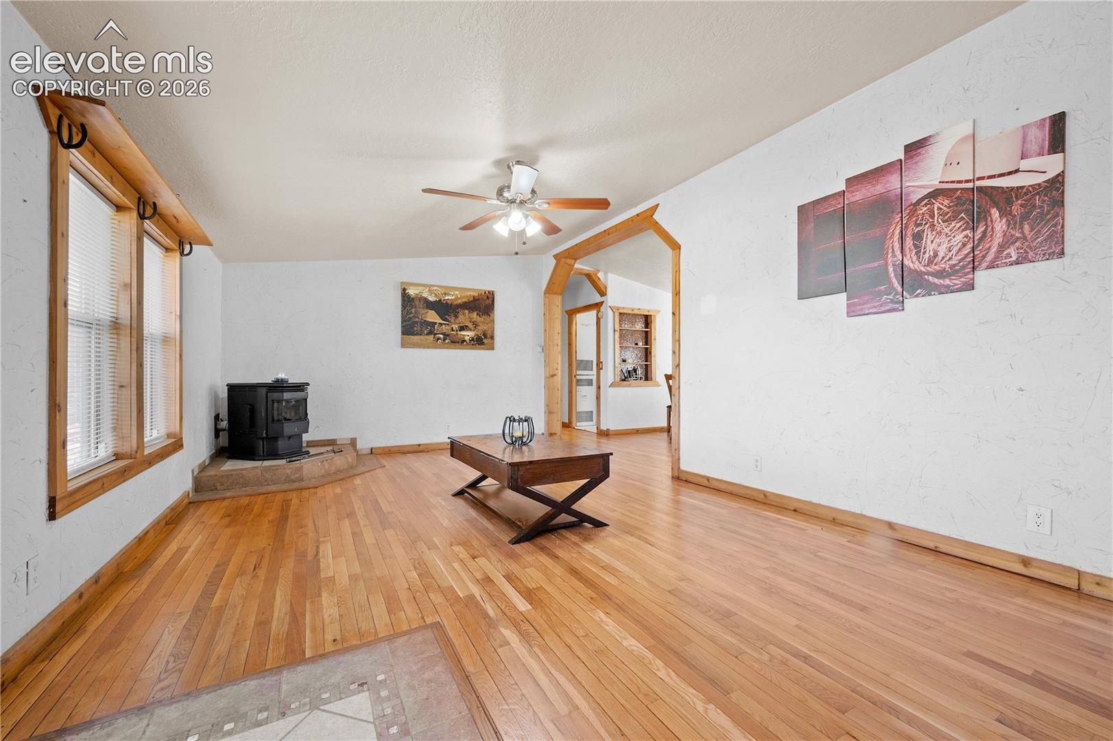 Unfurnished living room with lofted ceiling, wood-type flooring, a wood stove, and ceiling fan