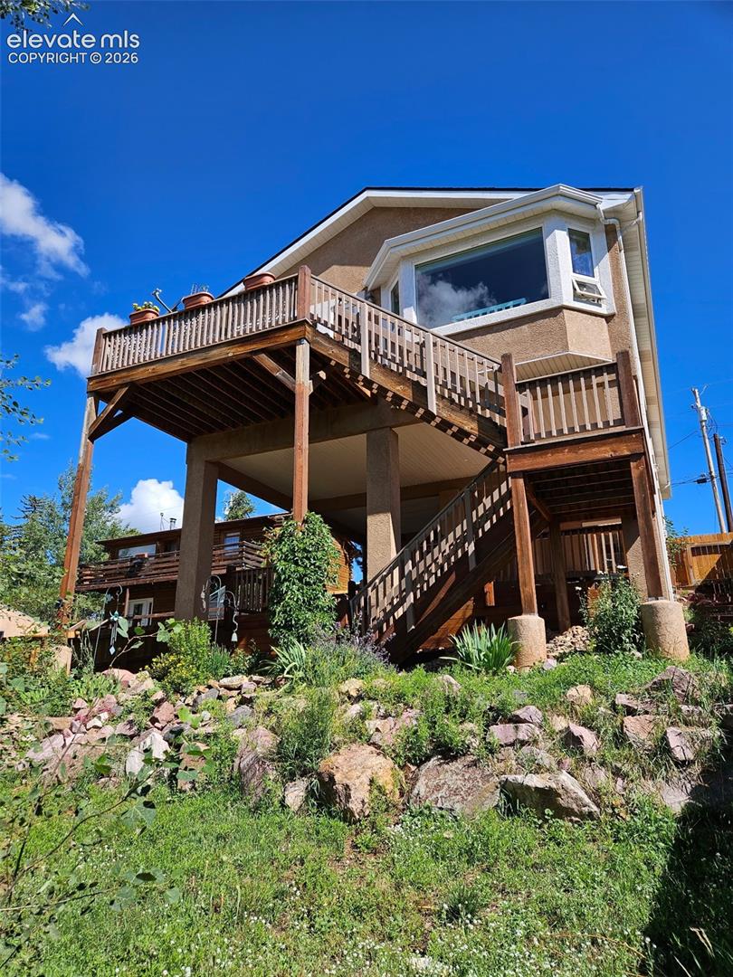 Multi-level exterior featuring a bay window, expansive wood deck, wood-railed staircase, and stucco siding