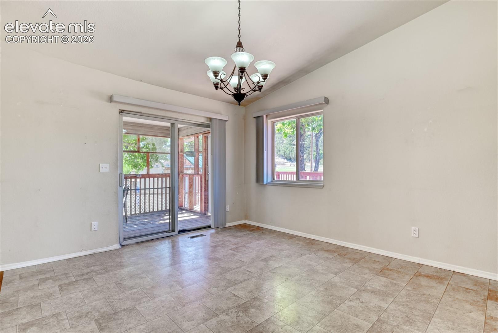 Vaulted ceiling with a multi-arm chandelier, tile flooring, and sliding glass door access to a covered outdoor area