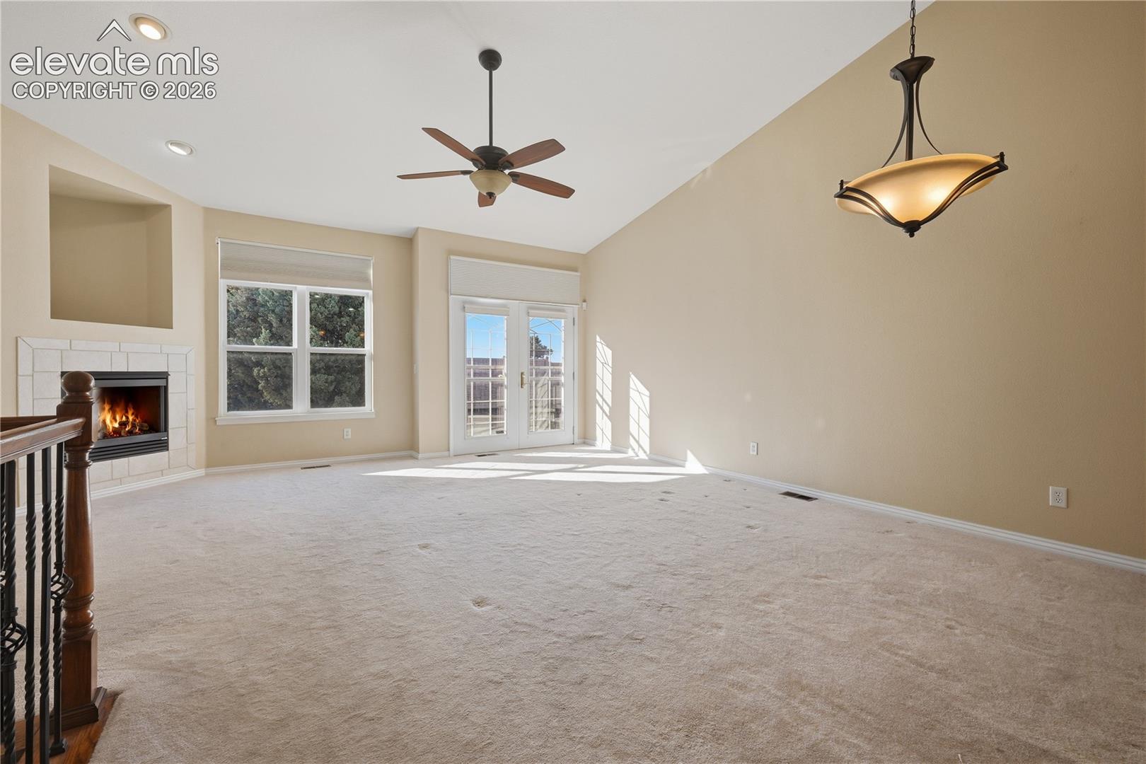 Vaulted ceilings, fireplace with tile surround, recessed lighting, multi-pane glass doors, and integrated ceiling fan