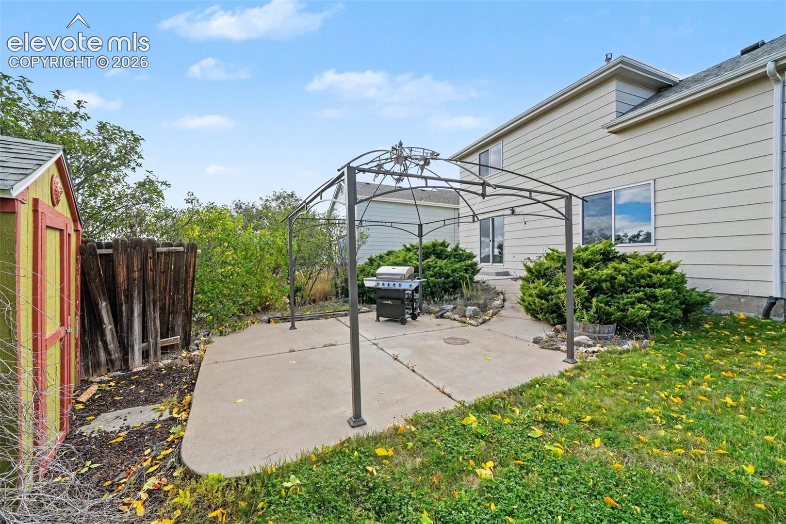 Backyard space featuring a concrete patio, metal frame gazebo, wood-sided exterior, and landscape shrubbery