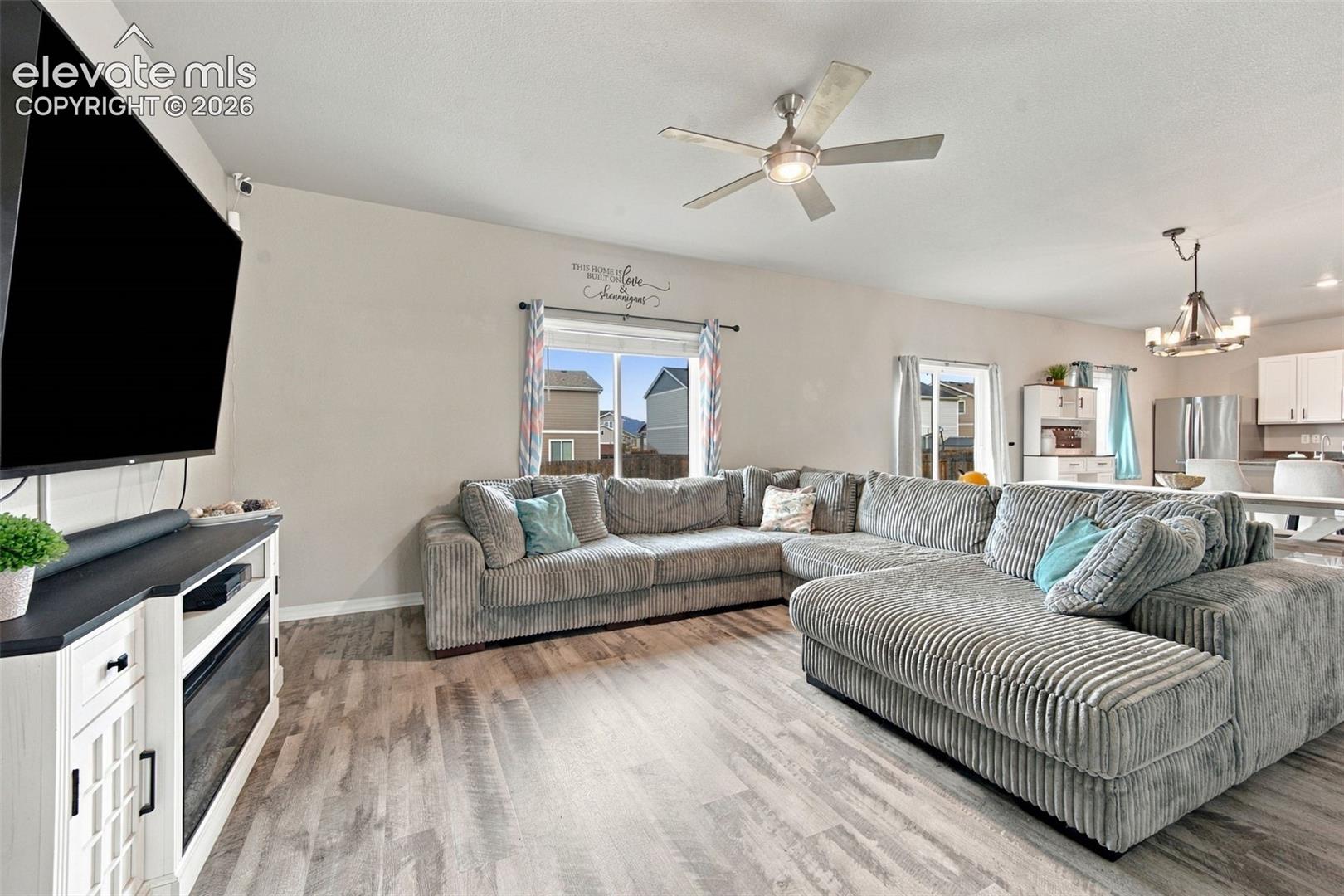 Open concept living area featuring wood-finish flooring, a ceiling fan with integrated lighting, a built-in electric fireplace console, and sliding glass doors