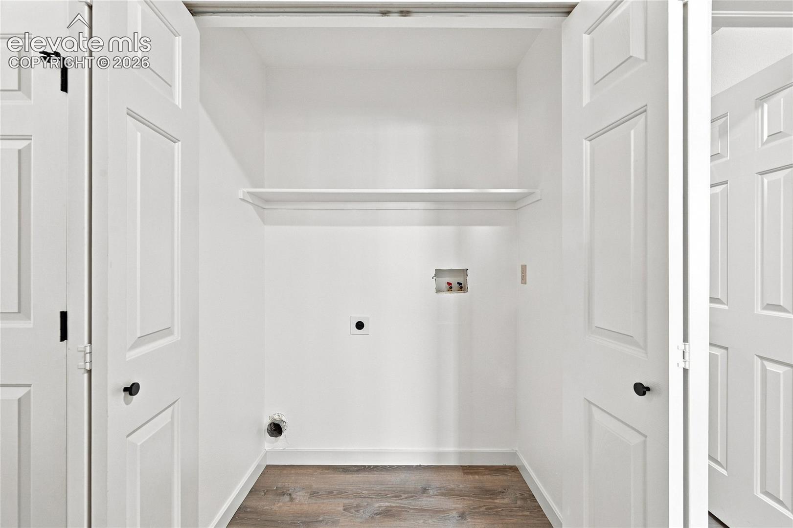 Laundry area featuring a built-in shelf, white paneled bifold doors, and wood-finish flooring