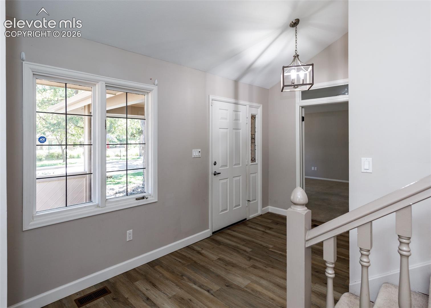 Vaulted entry with wood-finish flooring, white paneled entry door, and a decorative overhead light fixture