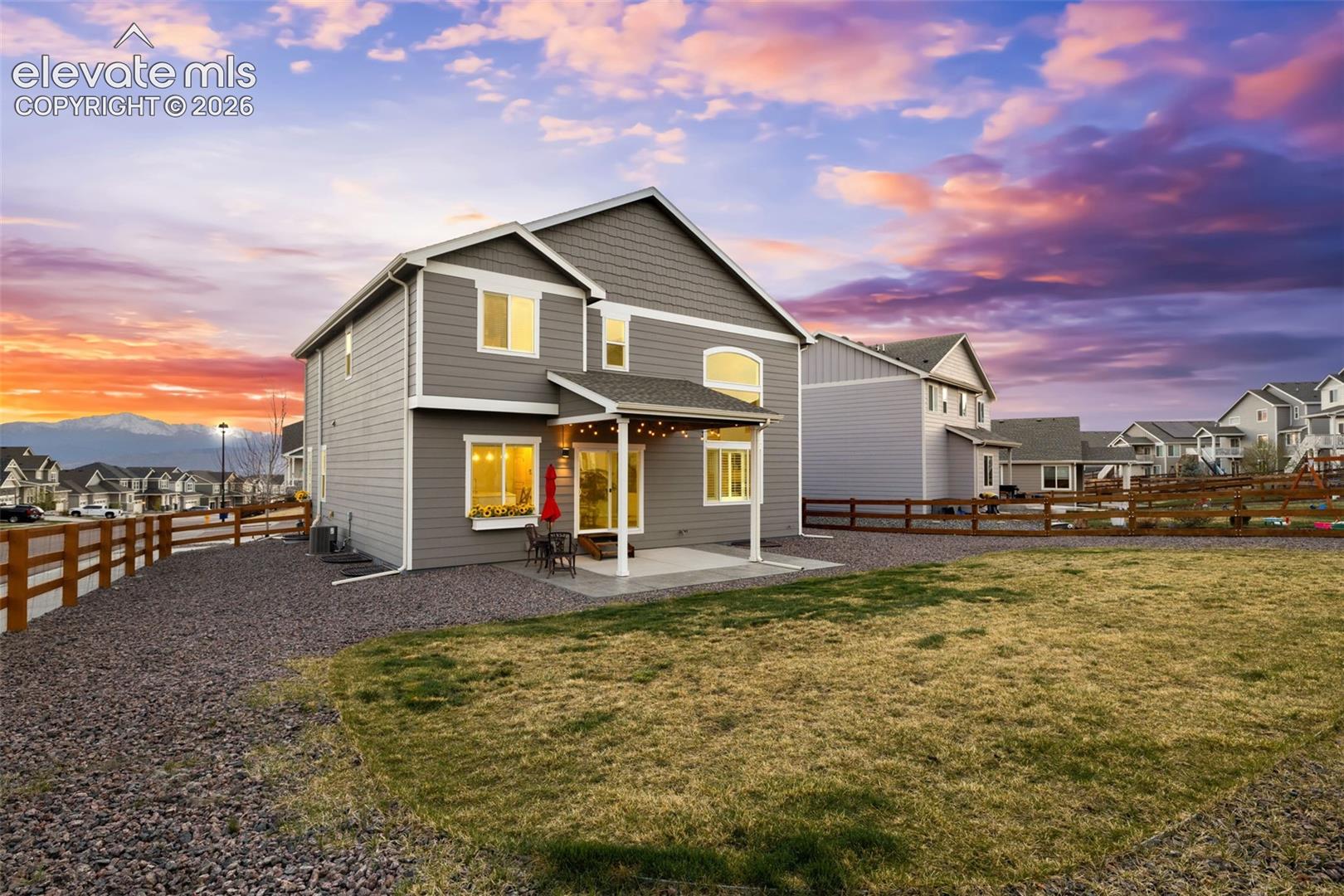 Two-story home with gray siding, covered patio, gravel landscaping, and a wood fence