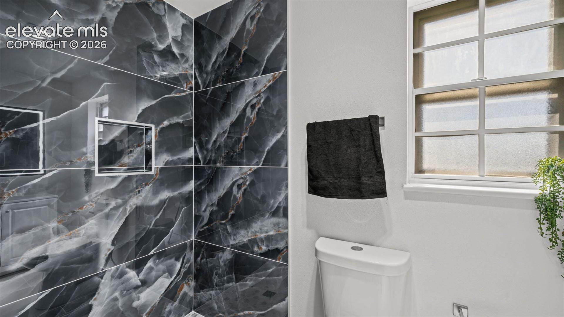 Large format dark grey veined tile, integrated shower niches, white framed window with privacy glass, white toilet fixture